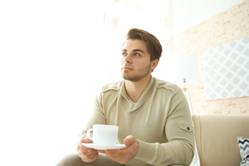 Handsome man drinking coffee on sofa in room
