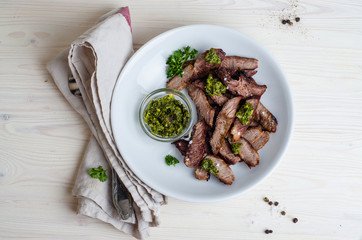 Sliced Steak served in white bowl with chimichurri sauce. Top view.