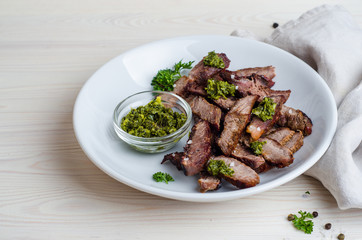 Sliced Steak served in white bowl with chimichurri sauce. Top view.