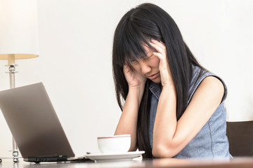 Asian Woman having a headache while she works on a laptop