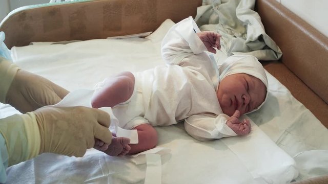 Nurse put on white disposable socks on newborn crying baby in diapers after birth. Maternity hospital.