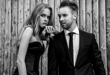 Portrait of young attractive couple posing outdoor against wooden background in black fashionable clothes. Black-white fashion photo.