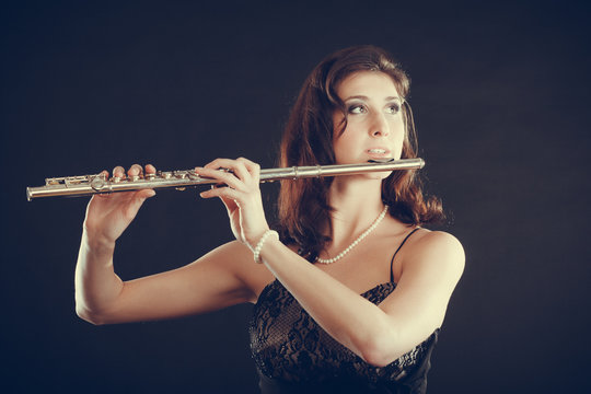 Woman playing transverse flute on black.