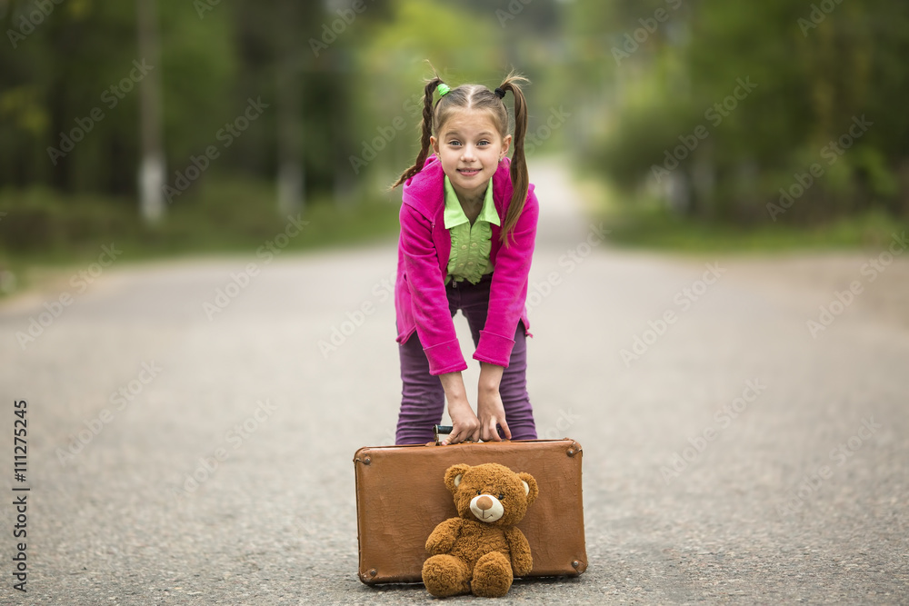 Wall mural naughty little girl with a suitcase and a teddy bear is going on a trip.