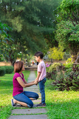 Mother sitting at park holding hands and teaching her son