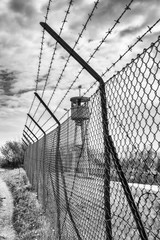 Abandoned sentry box tower isolated by a net with barbed wire. - obrazy, fototapety, plakaty
