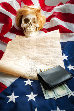 A human skull wearing a ginger wig on top of the US constitution and the upside down american flag symbolizing the danger that demagoguery, racism, manipulation and hatred can bring to freedom