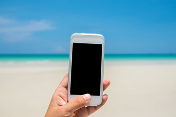 Woman hand hold white mobile phone with sea and blue sky