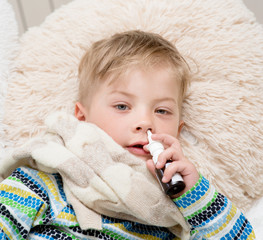 ill boy with flu at home using nose spray