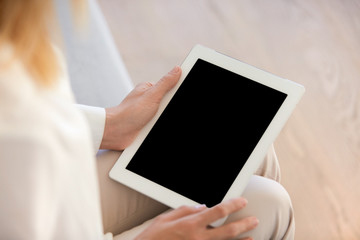 Young woman office worker holding electronic gadget, reading news or watching photographs on the Internet while sitting on the sofa, spending free time  at home during weekend. Selective focus