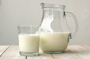 White milk in the glass with the jug on the wooden background