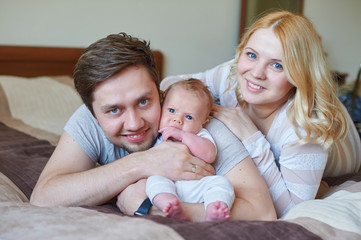 Beautiful happy couple and their baby relaxing in a bed together