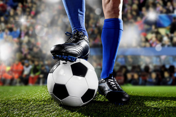 benen en voeten van voetballer in blauwe sokken en zwarte schoenen die staan met de bal die een wedstrijd speelt in het voetbalstadion