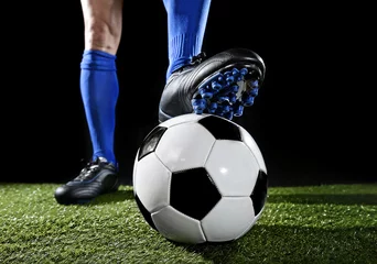 Foto op Plexiglas legs and feet of football player in blue socks and black shoes posing with the ball playing on green grass © Wordley Calvo Stock