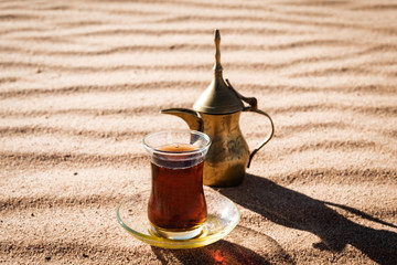 Arabic tea in traditional glasses and pot on desert at sunset, vintage style