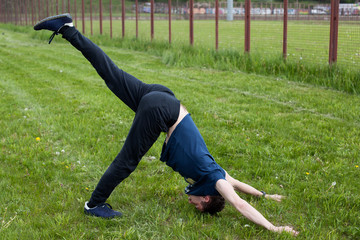 Fototapeta na wymiar Outdoor yoga workout. Young man doing an exercise in the city park, dog looking down pose