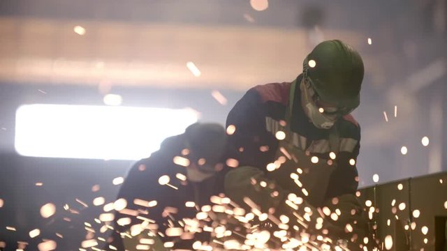 Worker using industrial grinder on metal parts in industrial workshop warehouse