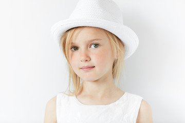 Lifestyle and people concept. Isolated headshot of beautiful Caucasian 5-year old female model with fair hair wearing stylish white clothes, looking and smiling at the camera with happy expression