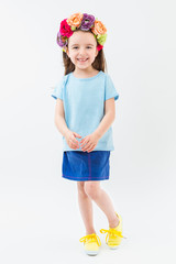 Flowers head accessory blue t-shirt navy skirt yellow sneakers casual style. No print clotes. Catalog template for branding. Smiling small kid girl. White background