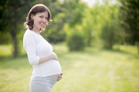 Happy pregnant woman on late pregnancy stage posing in park