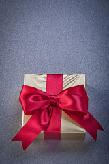 Present box wrapped in glittery paper with red bow on grey backg