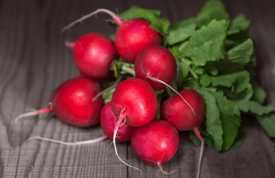 Ripe juicy red radishes with tops lying on wooden table.