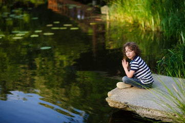 Pensive little boy sitting on the edge of the pond.