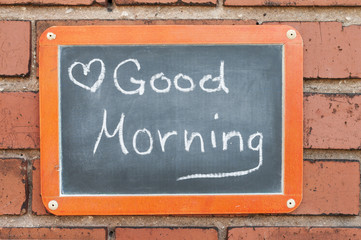 Tafel an einer Ziegelwand mit Text / Tafel an einer Ziegelwand mit Text Good Morning.