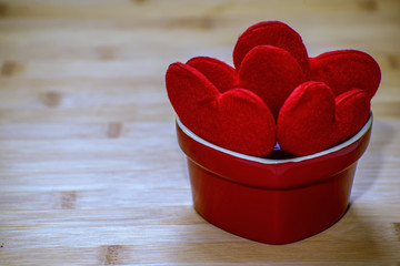 Heart shaped sweets wrapped in a bright red foil lying in a ceramic vase on a wooden texture. Background for romantic themes.
