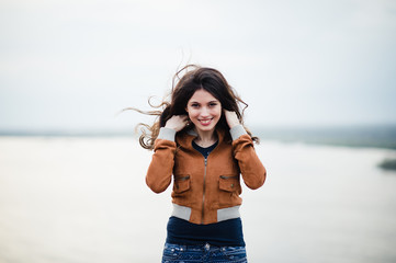 Young attractive happy girl with long hair smiling and posing outdoor. Wind blows her hair.