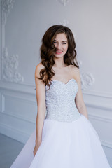 Close portrait of beautiful smiling bride woman with long curly hair posing in wedding dress at interior and smiling. Beauty indoor portrait.