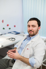 Calm doctor or consultant sitting at desk with his stethoscope on  table looking to the camera