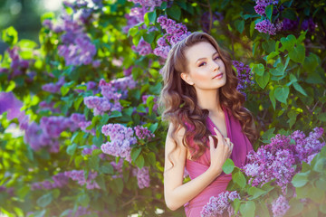 Young beautiful  girl posing near lilac bushes in blossom