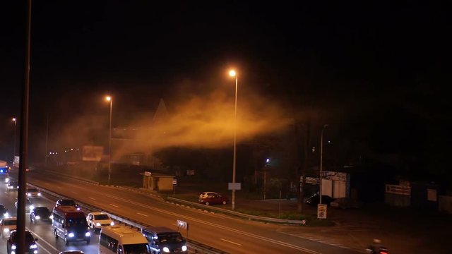 Cars driving slowly on highway, smoke from accident or fire floating above road
