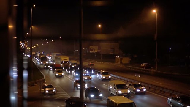 Various cars and trucks with lights on moving slowly in heavy traffic at night
