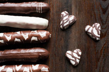 Set of different chocolate cookies, extreme close-up. Sweet chocolate cake sticks and hearts. Flat lay. Composition on dark wooden background