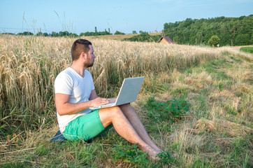 Naklejka na ściany i meble Rural guy with a laptop sitting near a wheat field