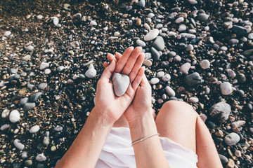 female  hands holding stone in the shape of a heart on the beach