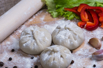 pile of homemade raw khinkali dumplings closeup with vegetables on the board