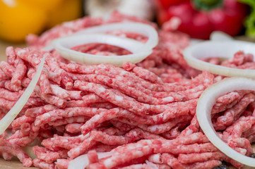 Raw minced meat and onion rings close-up with fresh vegetables on the background