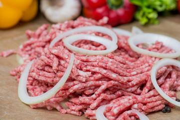 Raw minced meat and onion rings close-up with fresh vegetables on the background