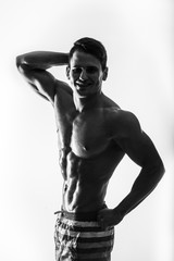 Dark contrast shot young muscular fitness man stomach and arm. Bodybuilder with beads of sweat training in gym. 