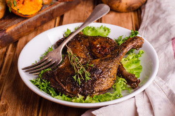 Confit duck legs with thyme in white plate on wooden background. Selective focus