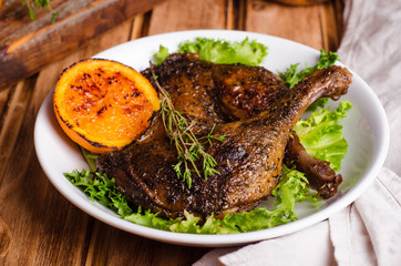 Confit duck legs with thyme in white plate on wooden background. Selective focus
