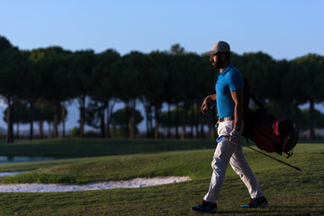Obraz premium golfer walking and carrying golf bag at beautiful sunset