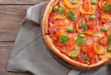 Tasty pizza with sausage and vegetables on burlap cloth and wooden table background