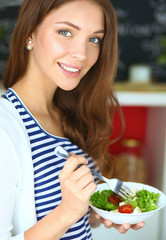 Young woman eating salad and holding a mixed salad 
