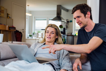 Joyful couple relax and work on laptop computer at modern living room at home. Guy is excited and pointing at computer.