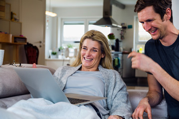 Man and woman laughing using laptop on couch at home