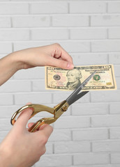 Hands with scissors cutting money on white brick wall background